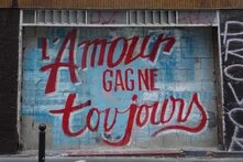 Graffiti an einer Hauswand, auf hellblauem Hintergrund steht in roter Schrift: L'Amour gagne toujours