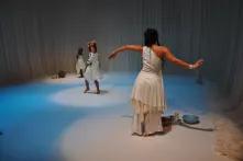 Bühnenbild von dem Stück "Caminho das Aguas", zu sehen sind drei Schwarze tanzende Frauen in weißen Kleidern