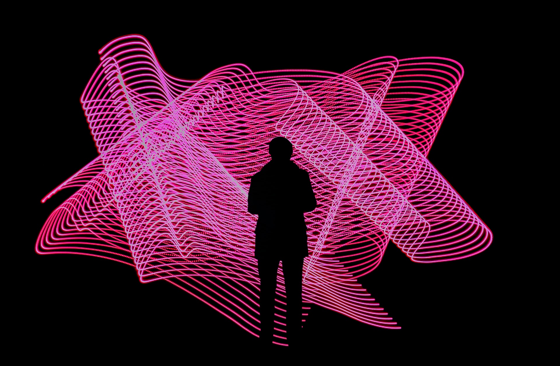 Schwarze Silhouette einer Person in schwarzer Umgebung steht vor pinker neon Installation