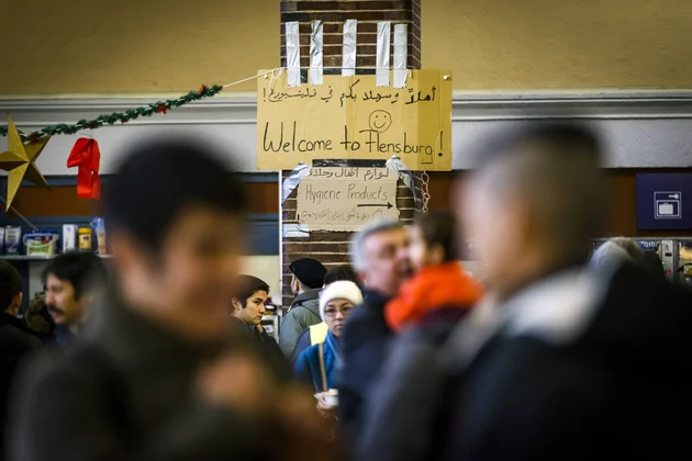 Mehrere Menschen in einer belebten Halle, im Hintergrund ein Schild mit „Welcome to Flensburg!“