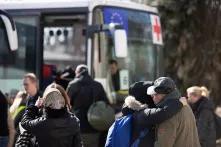 Evakuierung in Kyiv: Menschen umarmen und verabschieden sich, im Hintergrund ist ein Bus mit dem Symbol vom Roten Kreuz und der EU an der Frontscheibe zu sehen