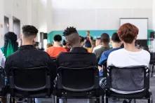Foto eines Klassenzimmers von hinten, in der letzten Reihe sitzen zwei Schwarze Jugendliche