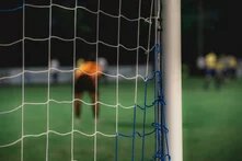 Fußballtor von hinten durch das Netz fotografiert, im Hintergrund sind etwas verschwommen Spieler zu sehen
