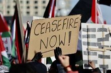 Bei einem Protest wird ein Schild mit der Aufschrift "Ceasefire Now!" hochgehalten, im Hintergrund sind palästinensische Flaggen zu sehen