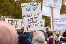 Bei einer Demonstration hält eine Person mit Kopftuch ein Schild hoch mit der Aufschrift "Redet nicht über uns, redet mit uns!!"