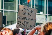 Auf einer Demo im Sommer 2024 wird ein Schild mit der Aufschrift "Aufstehen gegen Rechtspopulismus und seine Steigbügelhalter" hochgehalten.