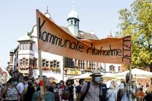 Zwei Personen in einer Menschenmenge halten ein großes Transparent fest mit der Aufschrift "Kommunale Aufnahme jetzt"
