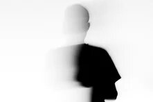 Eine verschwommene, mit dem weißen Hintergrund verschmelzende Silhouette eines Menschen