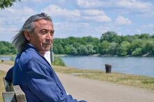 Ein Mann sitzt auf einer Bank an einem Fluss und schaut in die Ferne.