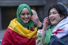 Foto: Zwei lachende Personen mit bemalten Gesichtern und Fahnen um die Schultern, eine hält eine Rose in der Hand.
