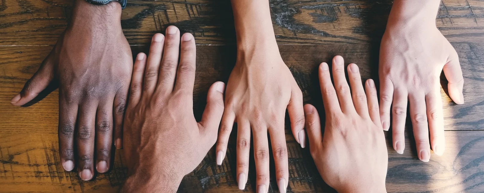 Fünf unterschiedliche Hände mit dem Handrücken nach oben auf einem Holztisch
