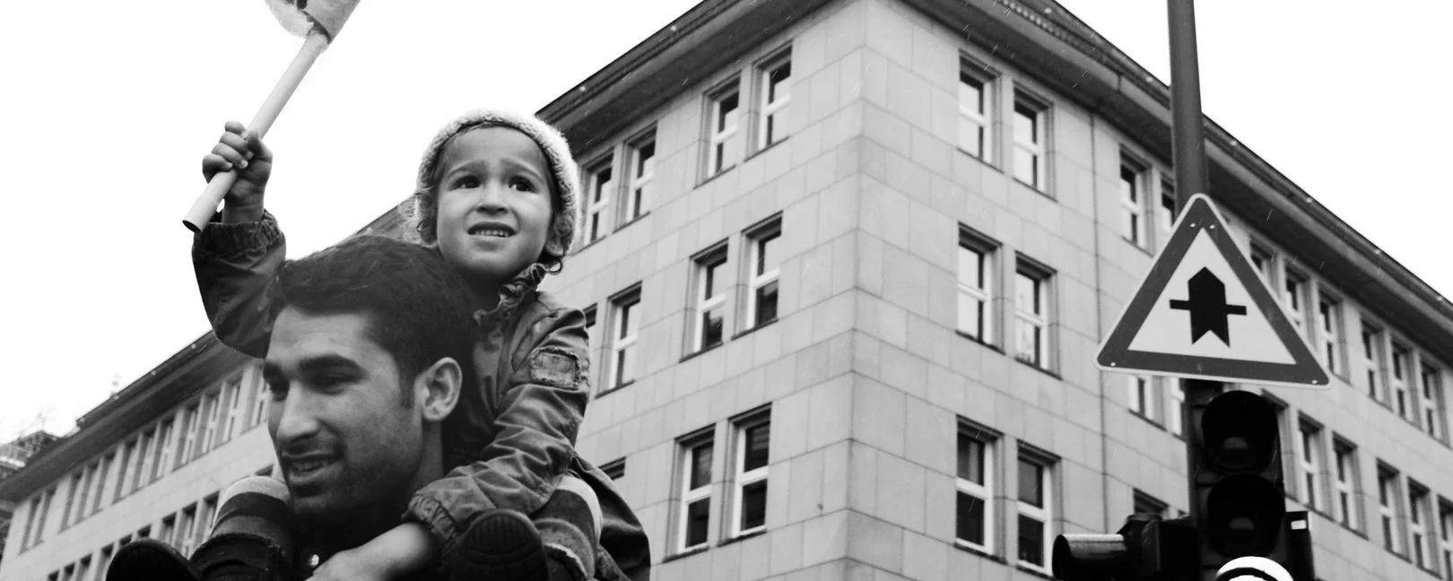 Schwarz-weiß Foto eines Mannes mit einem Kind auf den Schultern, das eine Fahne hochhält 