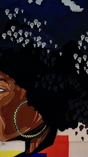 Wandbild einer Schwarzen Frau im Profil mit Afrofrisur, in und um den Haaren sind zahlreiche erhobene Fäuste zu sehen; links davon ist eine rote Rose abgebiledet, auf der "Rose City Justice" steht, signiert ist das Bild mit @empwo 
