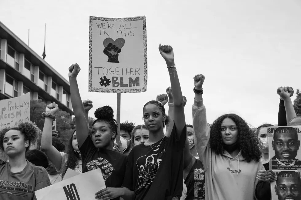 Junge Protestieren of Color halten Schild mit Aufschrift "We're all in this together, BLM" hoch