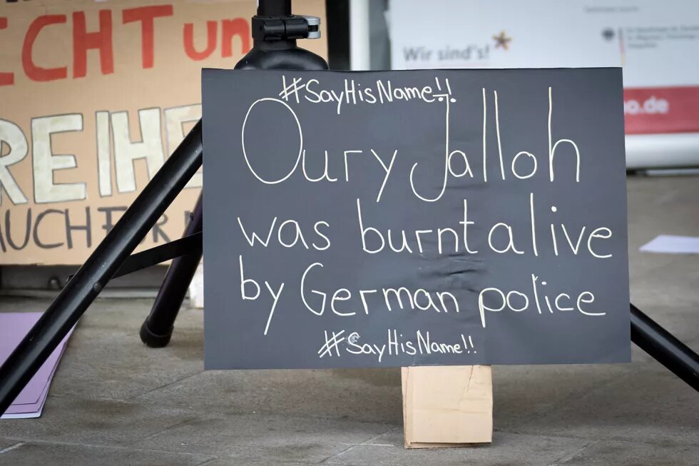 Schild mit Aufschrift "Oury Jalloh was burnt alive by German Police #SayHisName!"