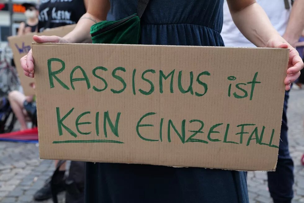 Pappschild mit grüner Aufschrift "Rassismus ist kein Einzelfall" auf einer Migrantifa Demo in Berlin