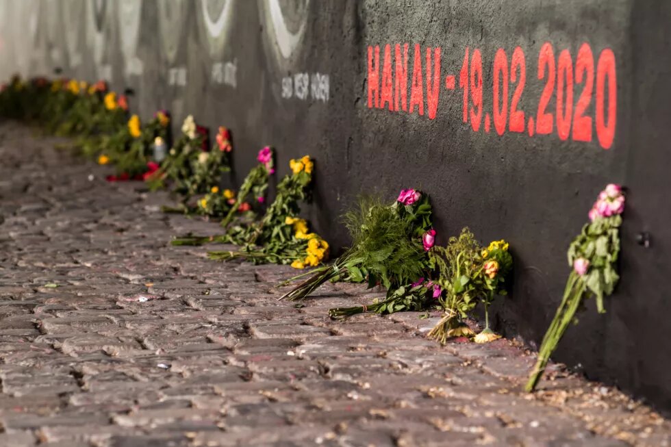 Blumensträuße vor dem Graffiti in Frankfurt in Gedenken an die Opfer in Hanau, zu lesen in roter Schrift "Hanau - 19.02.2020"