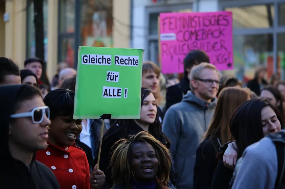 Bild einer Frauenkampftagsdemo, im Vordergrund zwei Schwarze Frauen, die ein Schild mit der Aufschrift "Gleiche Rechte für alle" hochhalten