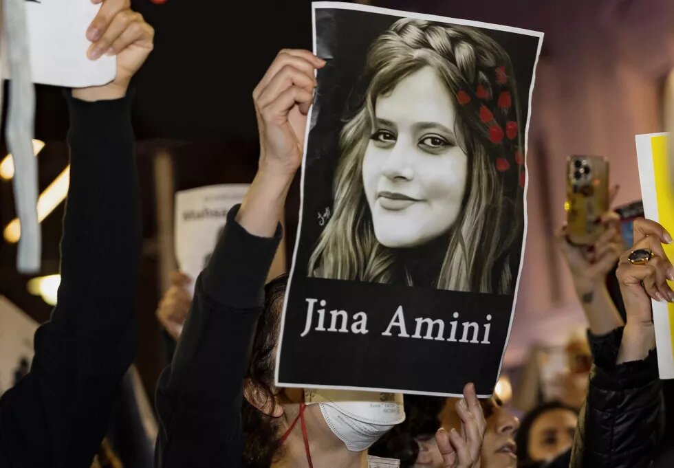 Bei einer Demonstration wird ein Bild einer Frau hochgehalten, darunter steht "Jina Amini".