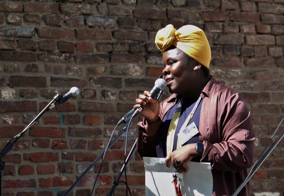 Foto von Emilene Wopana Mudimu mit einem Mikro in der einen und einem Blatt Papier in der anderen Hand