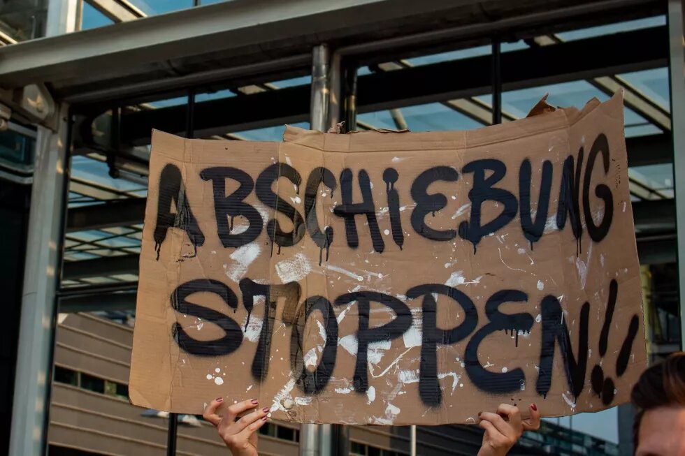 Zwei Hände halten ein Pappschild mit der Aufschrift "Abschiebung stoppen!!" hoch