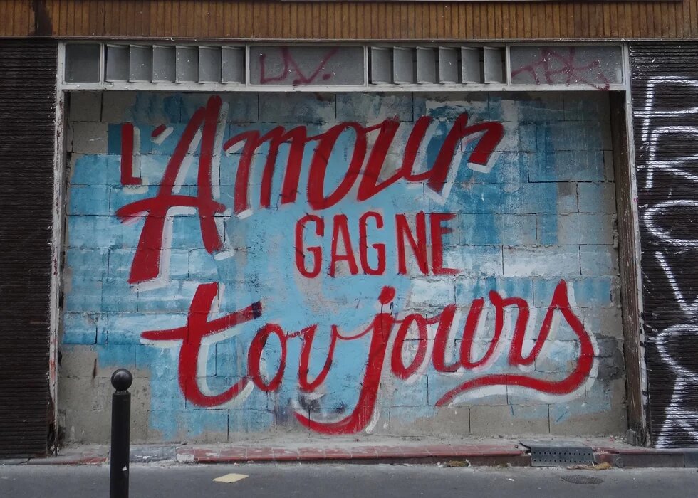 Graffiti an einer Hauswand, auf hellblauem Hintergrund steht in roter Schrift: L'Amour gagne toujours