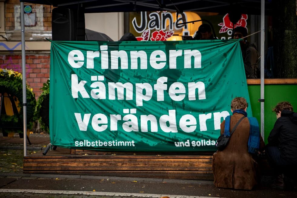 Bei einer Kundgebung zum Gedenken an den Anschlag in Halle ist ein großes Transparent zu sehen, auf dem "erinnern, kämpfen, verändern. selbstbestimmt und solidarisch" steht