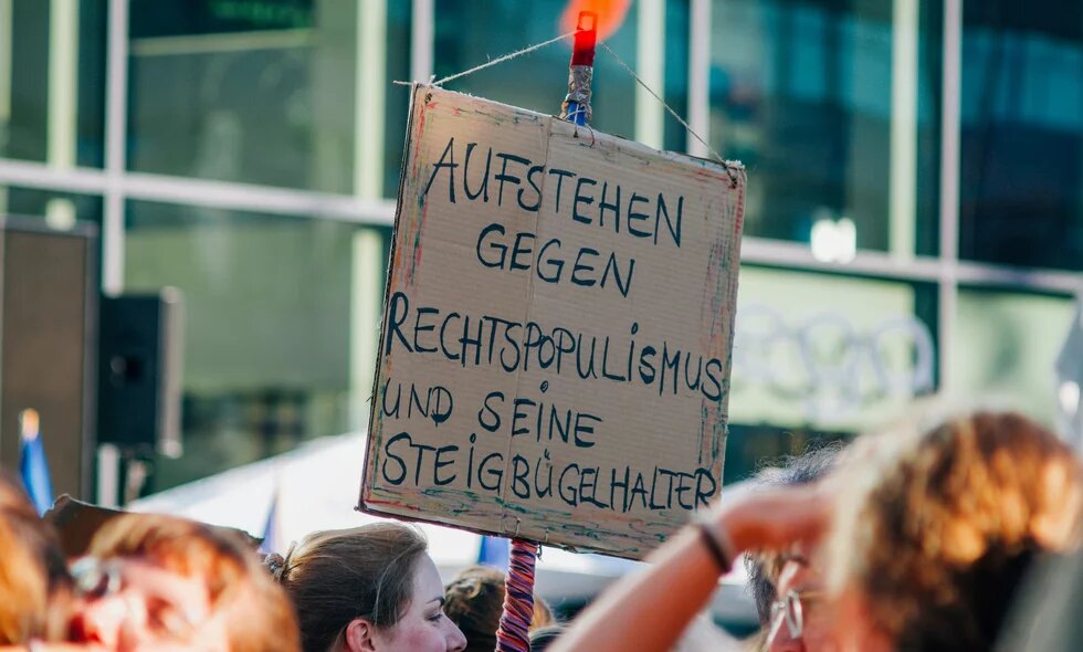 Auf einer Demo im Sommer 2024 wird ein Schild mit der Aufschrift "Aufstehen gegen Rechtspopulismus und seine Steigbügelhalter" hochgehalten.