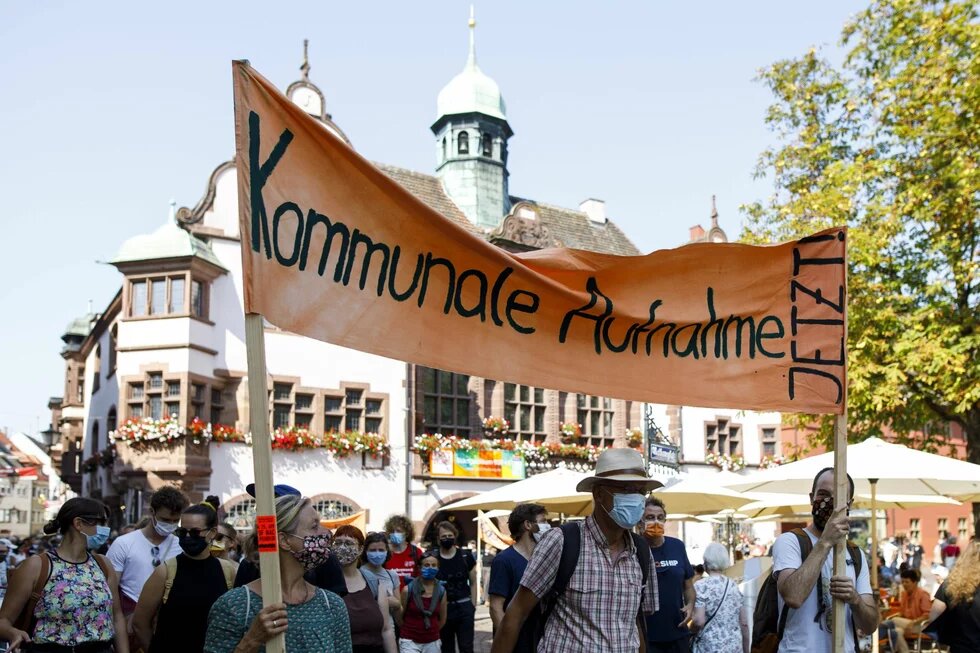 Zwei Personen in einer Menschenmenge halten ein großes Transparent fest mit der Aufschrift "Kommunale Aufnahme jetzt"