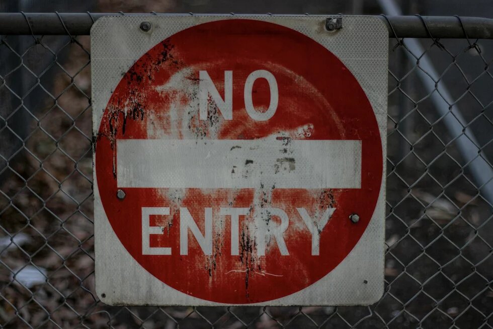 Rotes Einfahrtsverbotsschild mit der Aufschrift "No Entry", das an einem Zaun befestigt ist