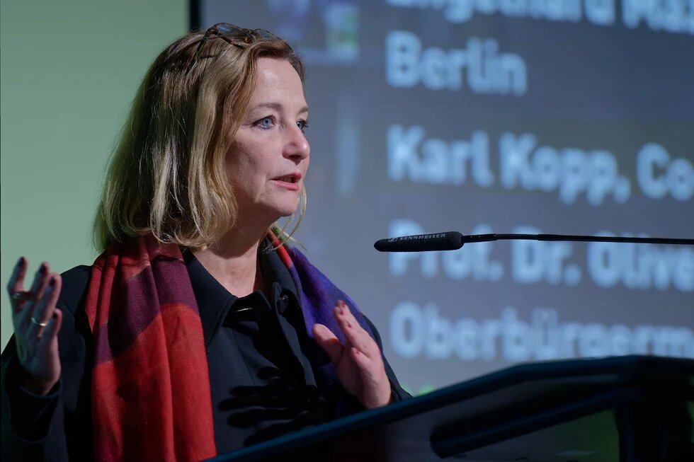 Petra Bendel steht an einem Rednerpult und spricht ins Mikrofon