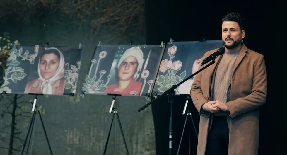 Ibrahim Arslan spricht bei einer Gedenkveranstaltung, neben ihm sind drei großformatige Fotos seiner beim Brandanschlag ums Leben gekommenen Angehörigen zu sehen. 