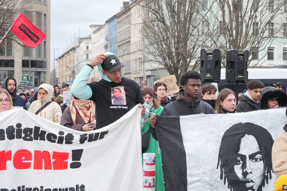 Auf einer Demonstration hält Suraj Mailitafi gemeinsam mit anderen Personen einen Banner mit einem Bild von Lorenz A. 