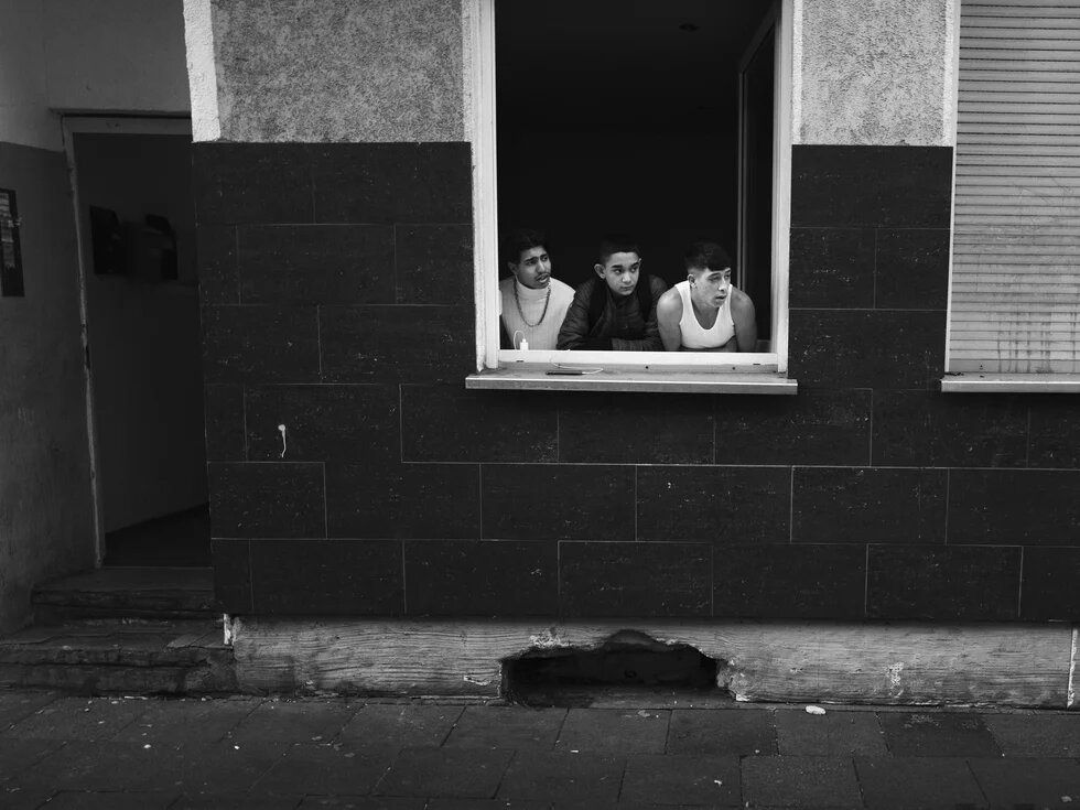 Schwarz-Weiß Fotografie von drei Jugendlichen, die aus dem Fenster auf die Straße schauen