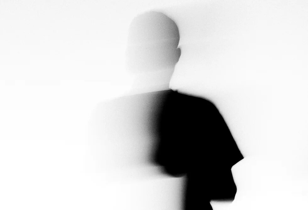 Eine verschwommene, mit dem weißen Hintergrund verschmelzende Silhouette eines Menschen