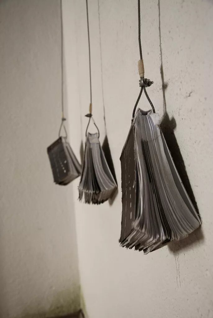 Drei Bücher die an Stahlseilen vor einer Wand hängen