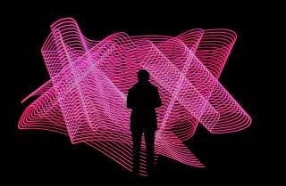 Schwarze Silhouette einer Person in schwarzer Umgebung steht vor pinker neon Installation