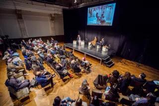 Veranstaltung 60 Jahre zuhause in Almanya, zu sehen ist der Theatersaal im Ballhaus Naunynstraße mit Publikum sowie das Podium mit Idil Baydar, Tuba Bozkurt und Imran Ayata.