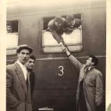 Altes Foto von mehreren Männern an einem Zug, zwei schauen aus dem Zugfenster, drei stehen davor; einer reicht einem draußen Stehenden aus dem Fenster zum Abschied die Hand