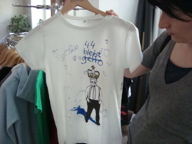 ruetli-wear Frau die ein weißes T-shirt Hochhält auf dem steht 44 bleibt getto
